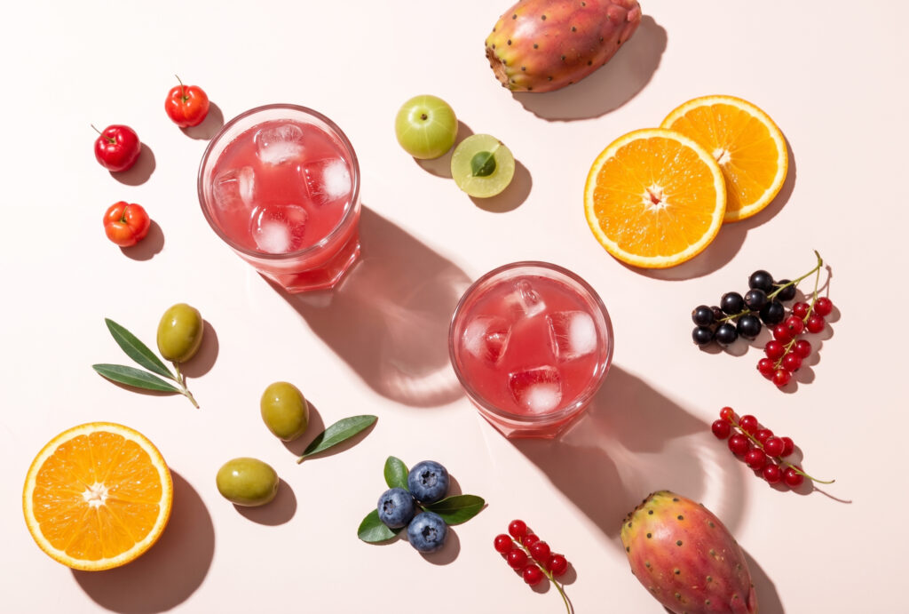 Two glasses of pink Collagen Phyto surrounded by antioxidant fruits